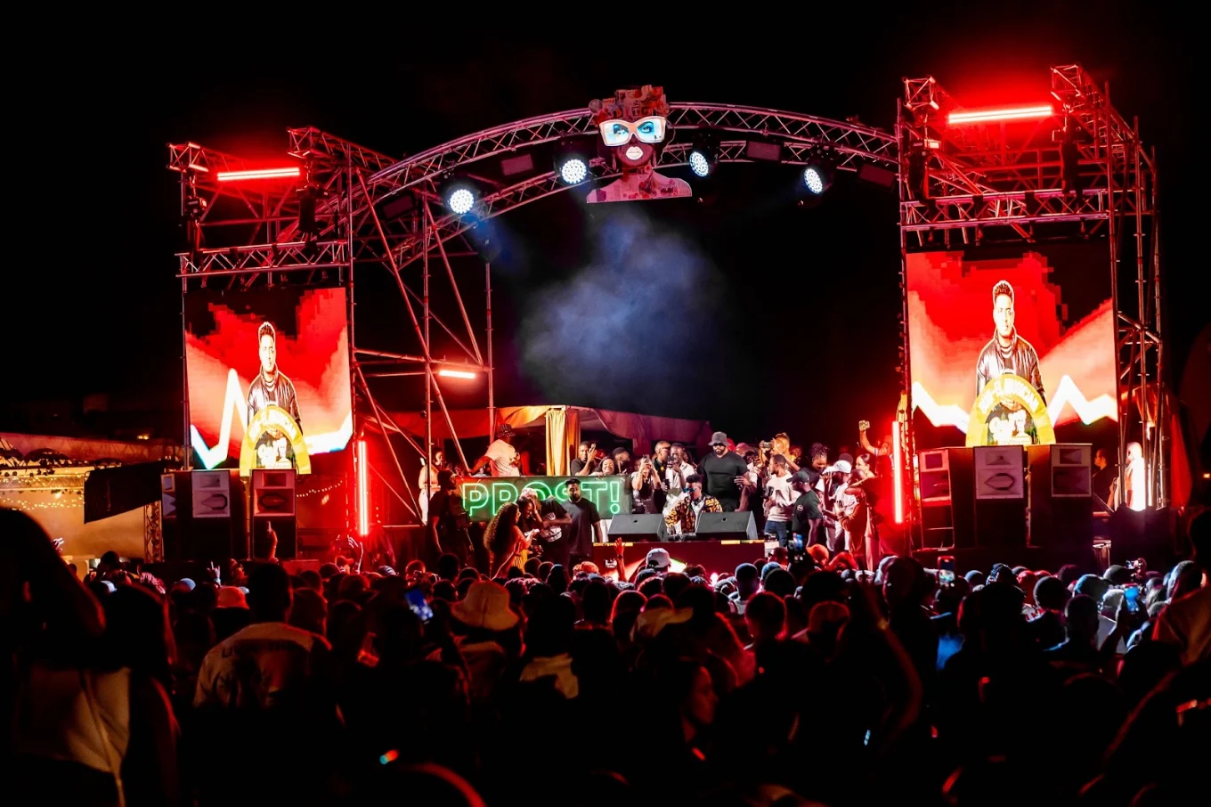 Crowd at a Plug & Play festival stage lit in red neon, DJ booth under trussing